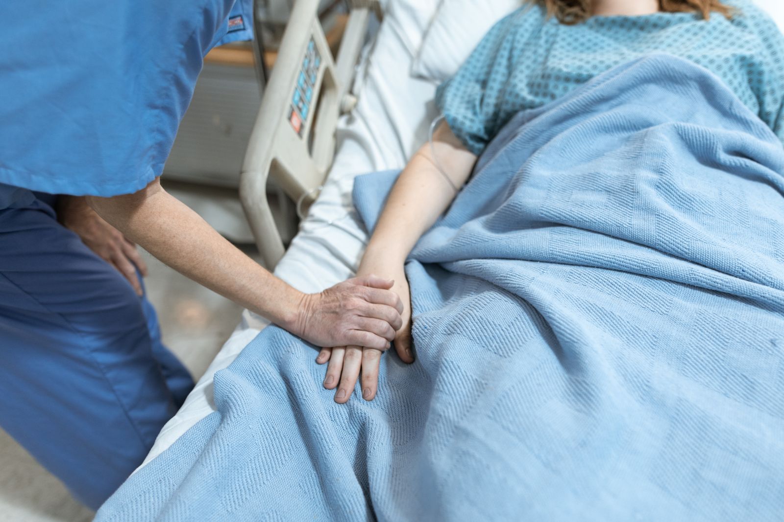 A nurse holding the hand of a patient in a hospital bed.